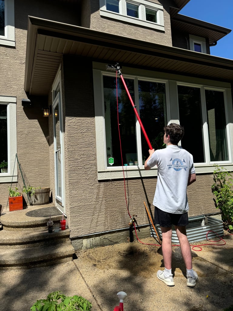 Person with pole cleaning large windows on modern brick house exterior on sunny day
