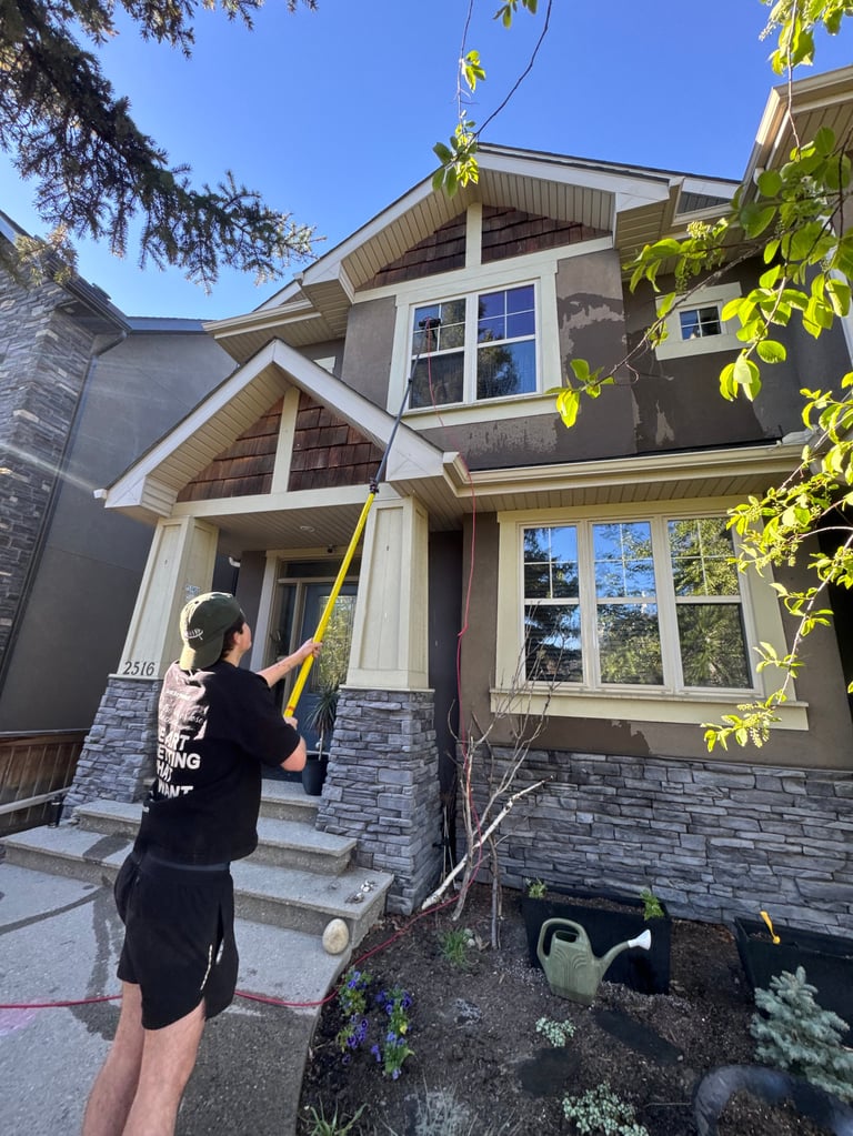 Person with a pole cleaning gutters on a two-story suburban house with stone and siding exterior