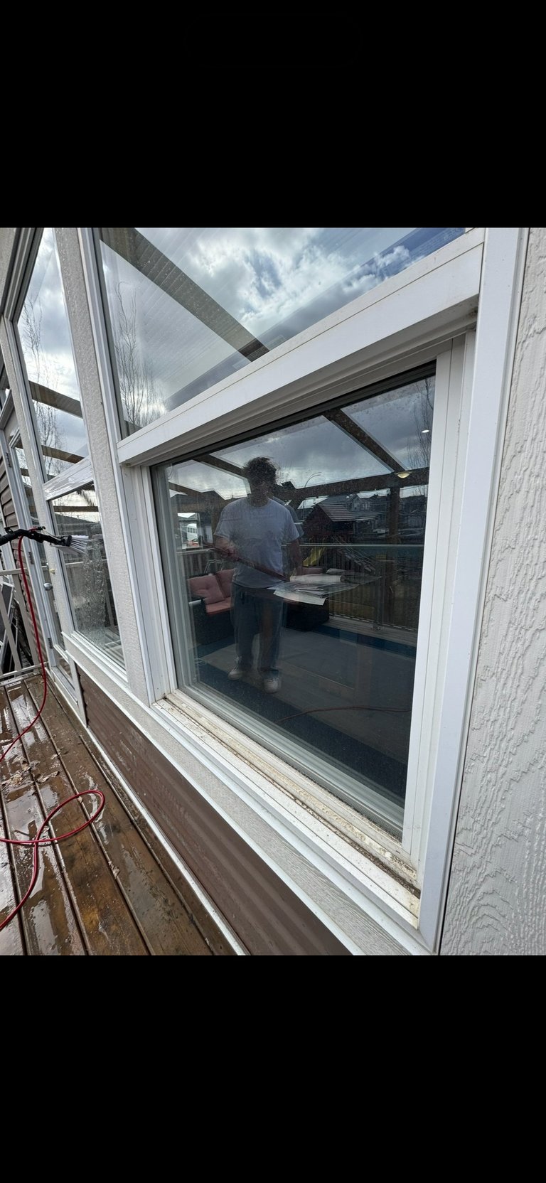 Modern white-framed glass conservatory with skylights overlooking garden, person visible inside standing by window