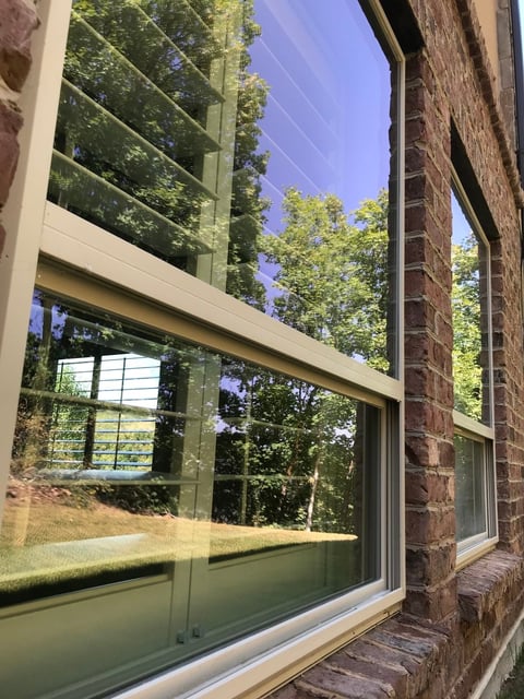 Large modern window with green frame in brick building overlooking forested landscape and clear blue sky