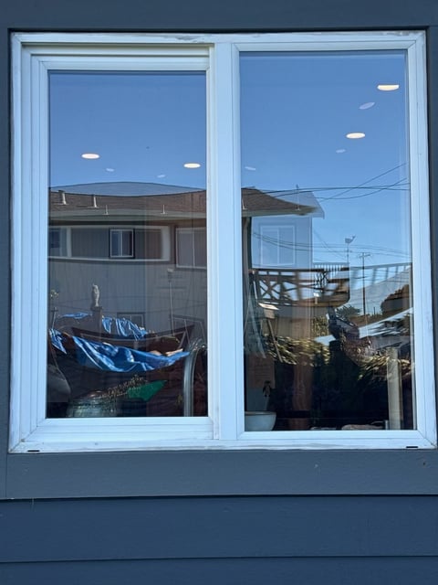 White-framed double window overlooking a residential area with boats and buildings reflected in the glass
