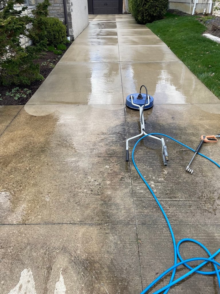 Pressure washer cleaning a wet concrete driveway with a blue hose coiled nearby