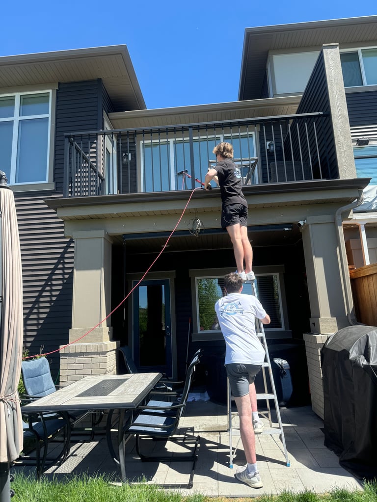 Two people practicing slack line on a residential deck with modern house and clear blue sky in background