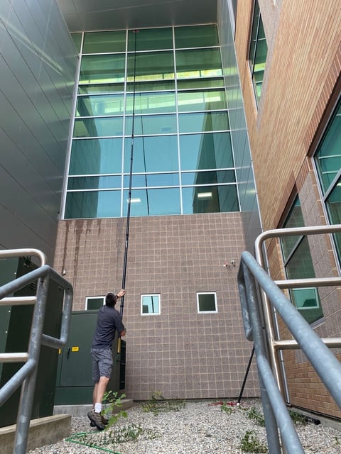 Person in dark jacket standing at entrance of modern brick building with large glass windows and metal railings