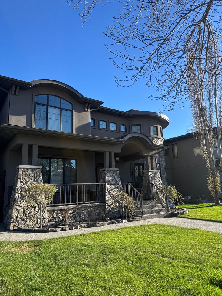 Modern two-story black house with curved windows, stone accents, metal railings, and manicured lawn under clear blue sky