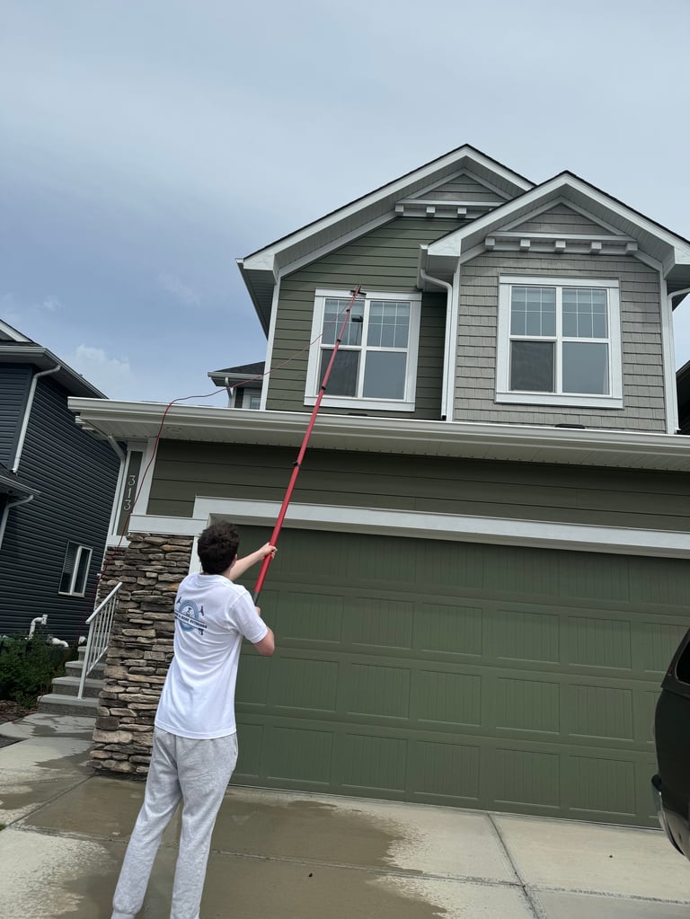 Person using a long-handled tool to clean the exterior of a two-story green house with a garage