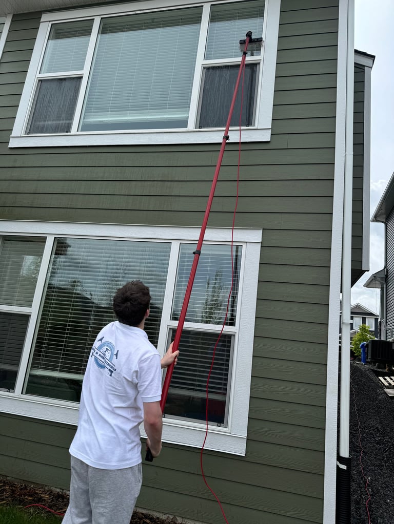 Man holding red pole extending from lower window to upper window on green house siding