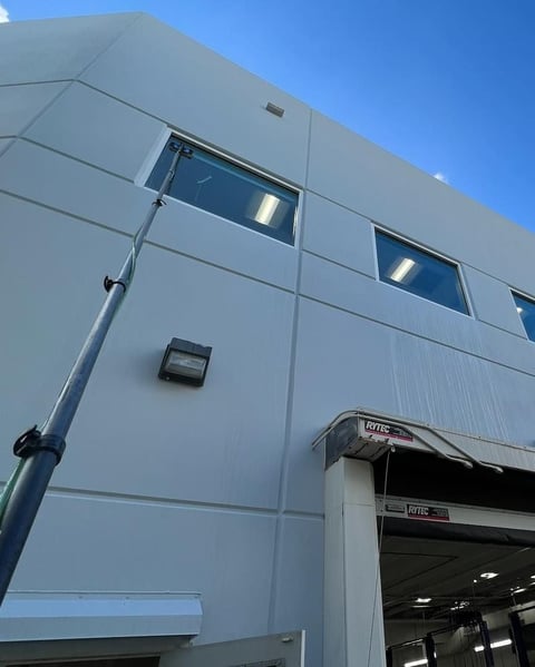 Modern white industrial building with two dark-tinted windows and an overhead garage door against a clear blue sky