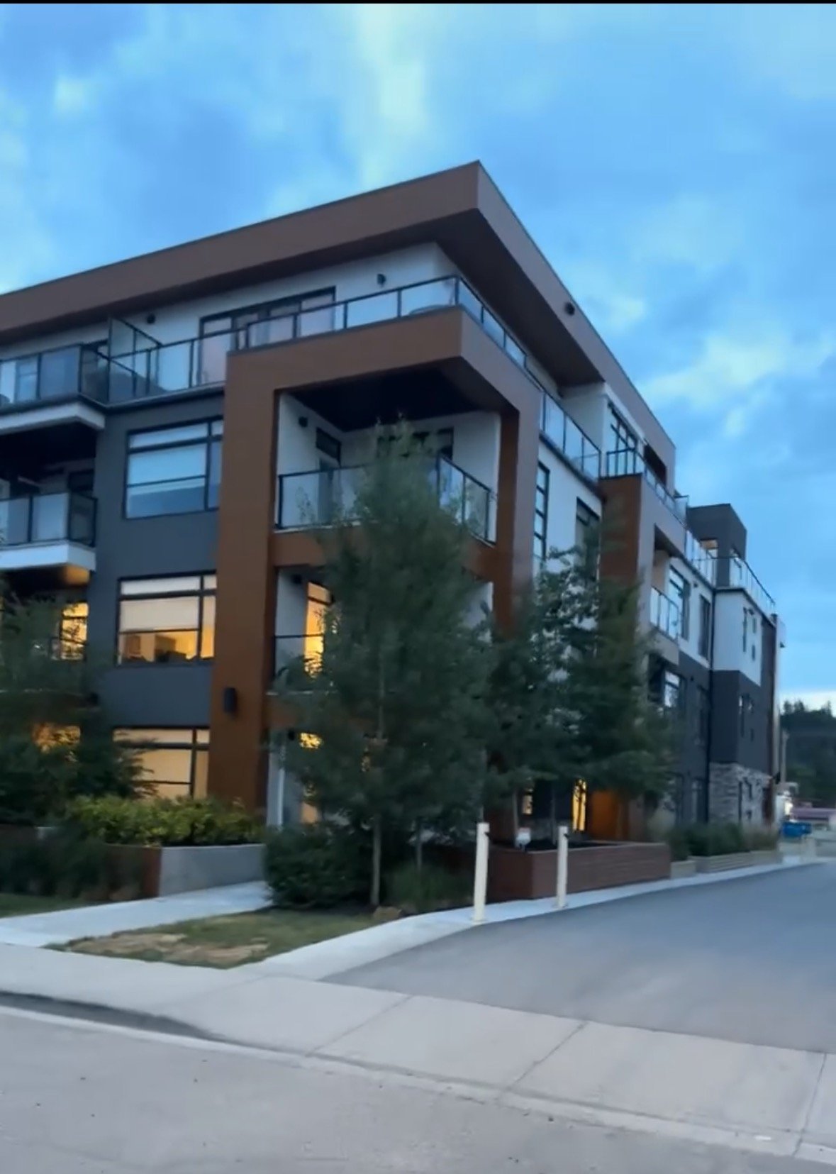 Modern multi-story residential building with bronze and dark exterior, large windows, and landscaping at dusk