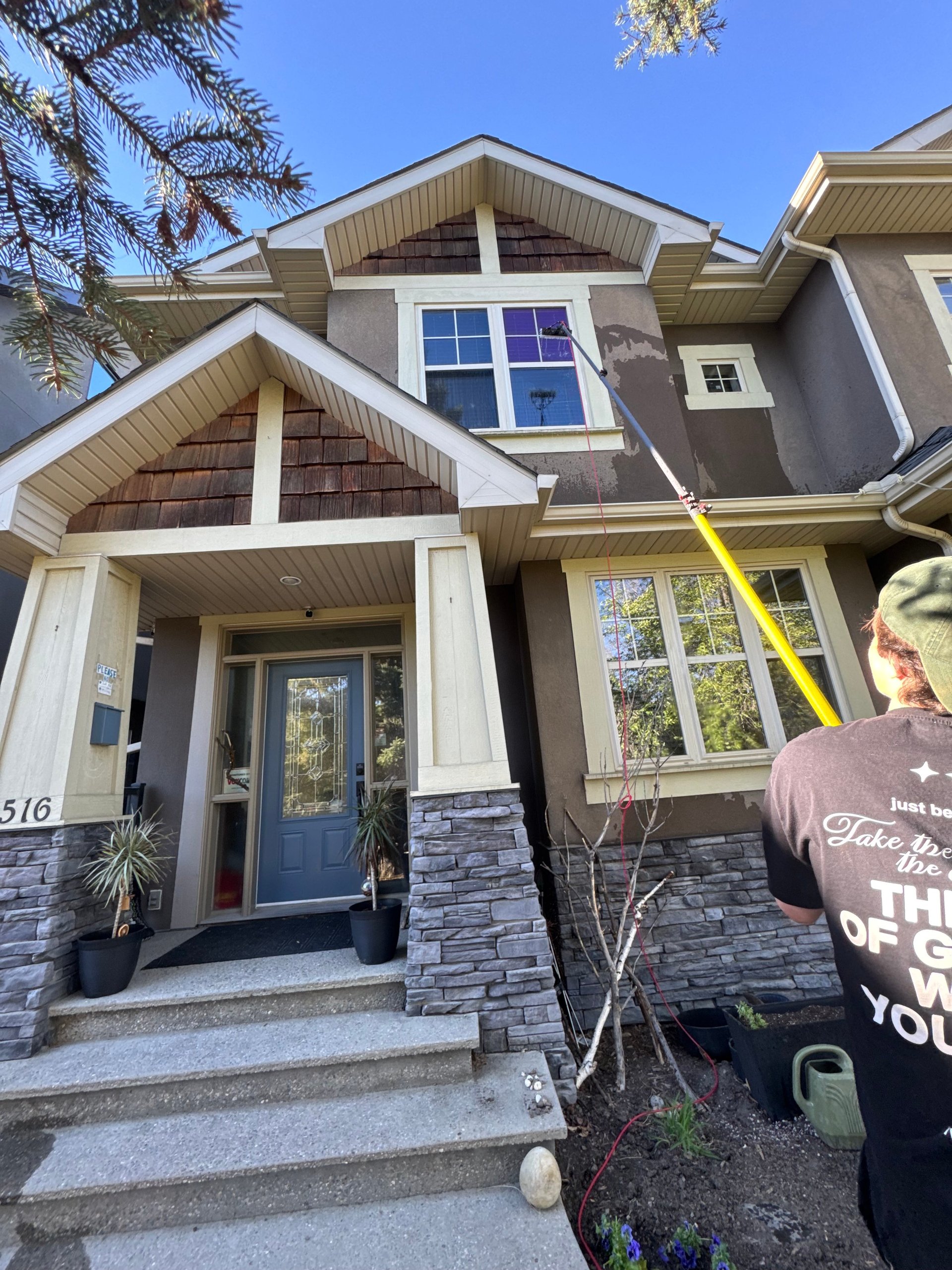 Modern two-story house with stone and stucco exterior, blue front door, and gabled roofline under clear blue sky