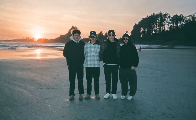 Five people standing together on a beach at sunset with forested coastline in the background