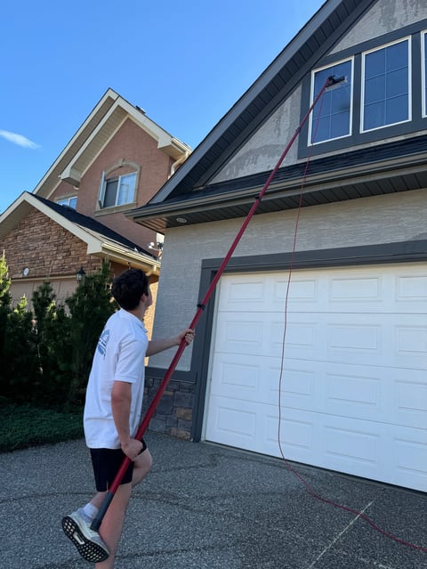 Person in white shirt holding a long red rope in front of a two-story brick and stone house with a white two-car garage door